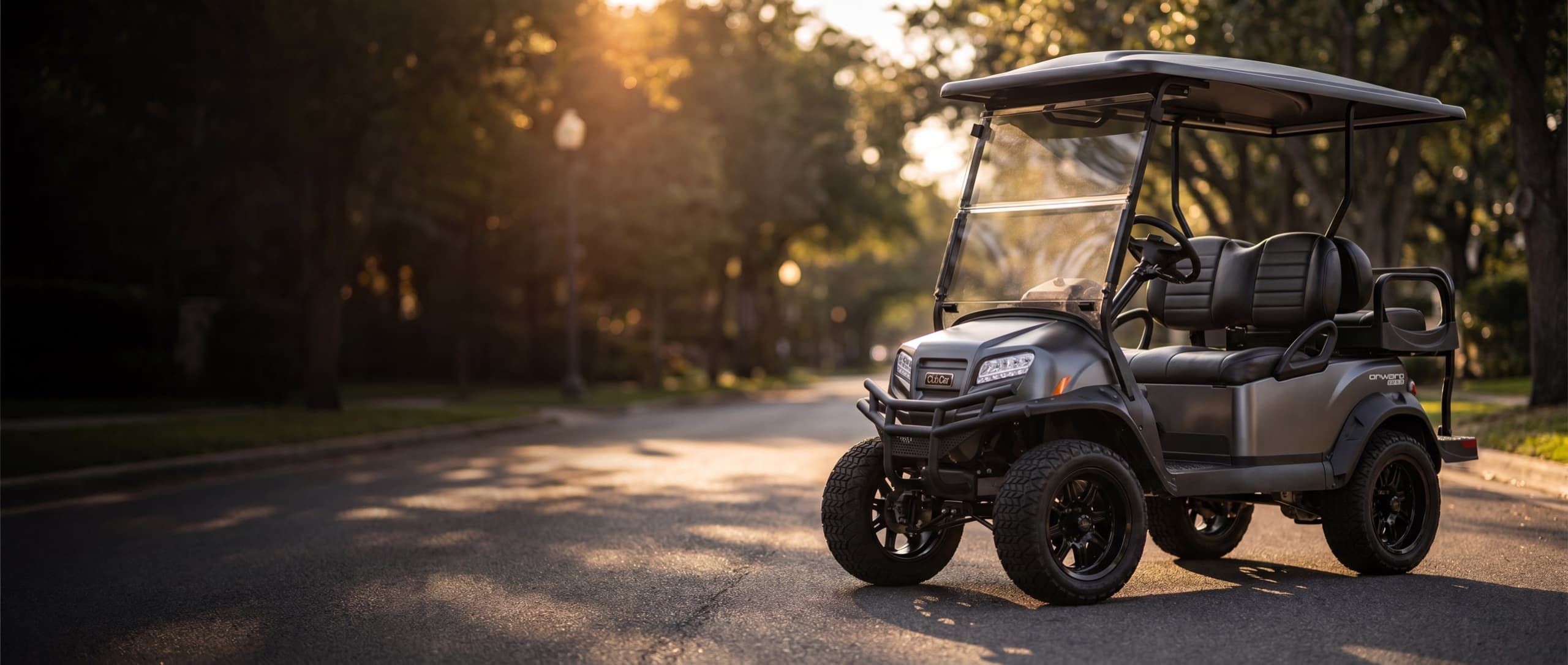 A matte-graphite lifted custom Club Car Onward on a tree-lined street at golden hour
