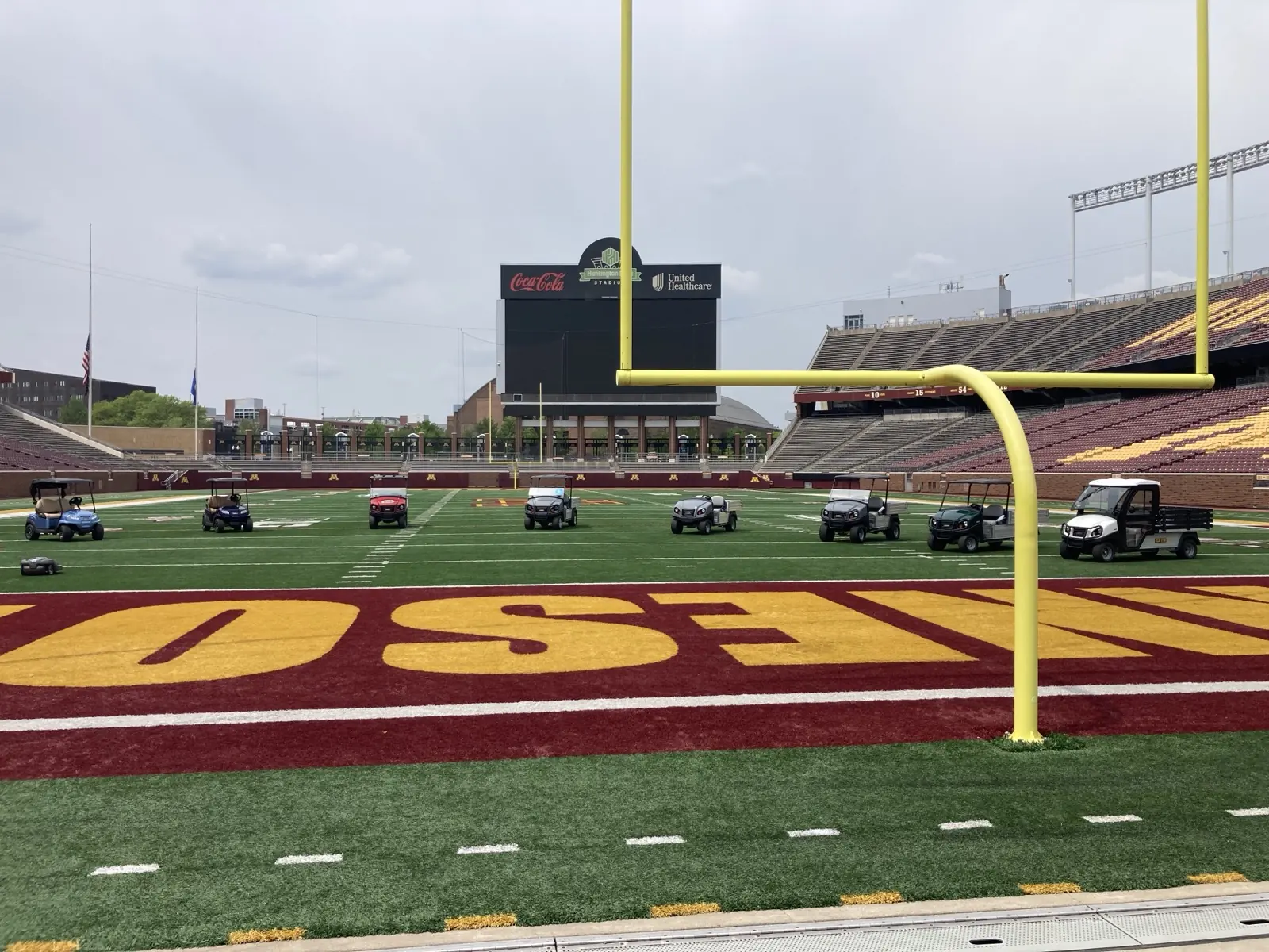 A wide view of Club Car utility vehicles, passenger carts, and a Husqvarna commercial robotic mower positioned across the football field at the University of Minnesota